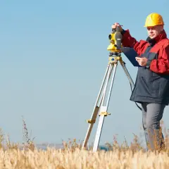 Geodeta w żółtym kasku pracuje przy niwelatorze. Zastanawiasz się, ile kosztuje geodeta przy budowie domu?