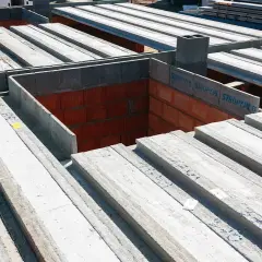 Budowa domu w toku: betonowe belki stropowe czekają na montaż, tworząc solidny strop nad ceglanymi ścianami.