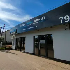 Nowoczesny budynek z dużymi oknami i drzwiami, z banerem "DRZWI OKNA BRAMY".