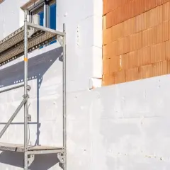 Budowa domu w toku: biały styropian 10 cm ile w paczce, rusztowanie i cegła.