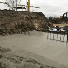 Świeża wylewka betonowa na zewnątrz, zbrojenie i koparki w tle.