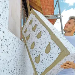 Budowlaniec montuje styropian na ocieplenie domu. Płyta z zaprawą gotowa do przyklejenia.