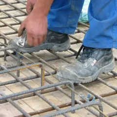 Pracownik w niebieskich spodniach i roboczych butach wiąże zbrojenie pod strop monolityczny.