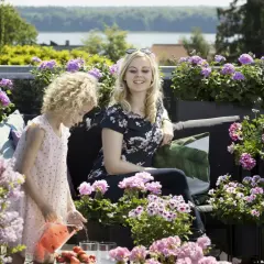 Kobieta i dziecko na tarasie wśród kwitnących pelargonii. Najpiękniejsze odmiany tworzą barwną oprawę letniego popołudnia.