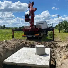 Montaż szamba betonowego w wykopie. Dźwig z ciężarówki przygotowuje się do pracy.