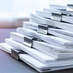 Stos dokumentów, które mogą dotyczyć podatku od działki budowlanej, spiętych metalowymi klipsami.