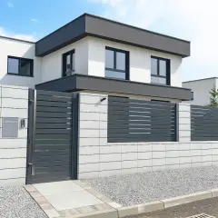 Nowoczesny dom z szarym ogrodzeniem lamelowym i betonowym murkiem. Idealny pomysł na ogrodzenie domu, który łączy styl i funkcjonalność.