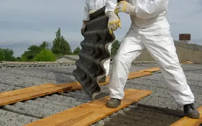 Osoby w kombinezonach ochronnych demontują eternit. Dowiedz się, ile kosztuje utylizacja eternitu i jak bezpiecznie usunąć ten materiał.