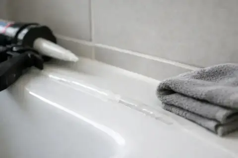 Pistolet do silikonu i szara ściereczka obok świeżo nałożonej spoiny. Czekamy, aż silikon schnie.