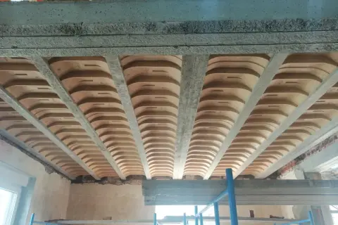 Widok od dołu na strop żelbetowy z pustakami ceramicznymi, tworzący charakterystyczny falisty wzór.
