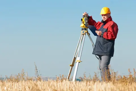 Geodeta w żółtym kasku pracuje przy niwelatorze. Zastanawiasz się, ile kosztuje geodeta przy budowie domu?