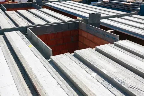 Budowa domu w toku: betonowe belki stropowe czekają na montaż, tworząc solidny strop nad ceglanymi ścianami.