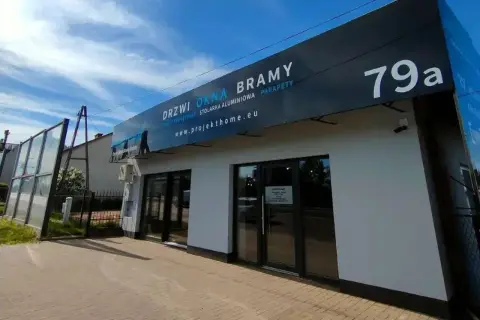 Nowoczesny budynek z dużymi oknami i drzwiami, z banerem "DRZWI OKNA BRAMY".