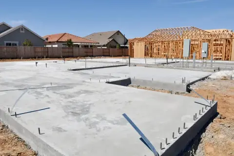 Fundament domu z chudego betonu, gotowy pod budowę ścian. W tle widać konstrukcję szkieletową domu.