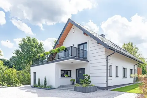 Nowoczesny biały dom z balkonem i zielenią. Idealny przykład, jak mogą wyglądać darmowe projekty domów.