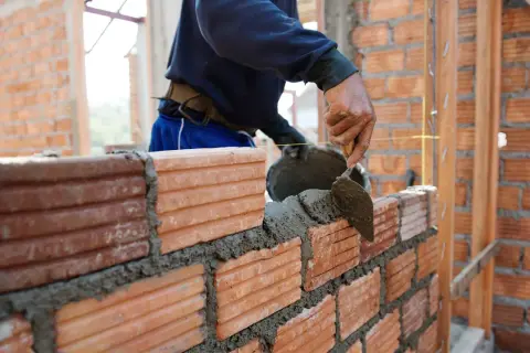 Murarz układa cegły, tworząc ścianę. Sprawdź, jaka jest murowanie ścian cena za m2 robocizna.
