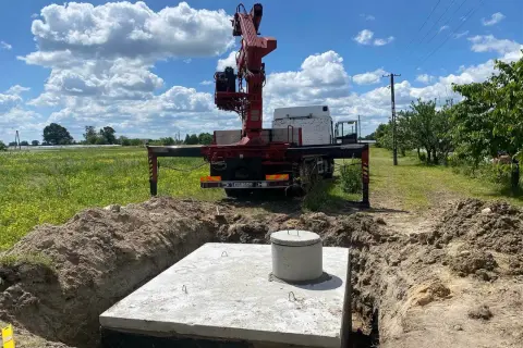 Montaż szamba betonowego w wykopie. Dźwig z ciężarówki przygotowuje się do pracy.