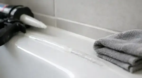 Pistolet do silikonu i szara ściereczka obok świeżo nałożonej spoiny. Czekamy, aż silikon schnie.