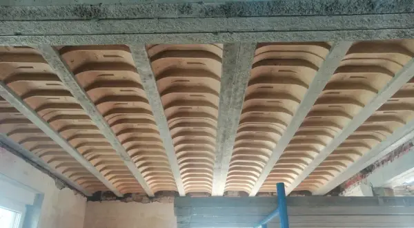 Widok od dołu na strop żelbetowy z pustakami ceramicznymi, tworzący charakterystyczny falisty wzór.