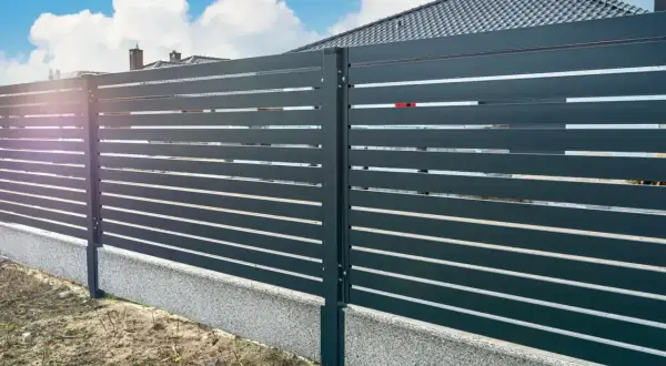 Nowoczesne ogrodzenie z poziomych paneli, osadzone na betonowym cokole. To świetne rozwiązanie, co zamiast podmurówki pod ogrodzenie, zapewniające estetykę i trwałość.