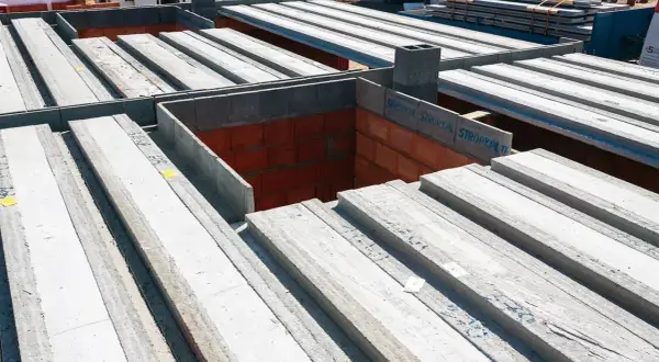 Budowa domu w toku: betonowe belki stropowe czekają na montaż, tworząc solidny strop nad ceglanymi ścianami.