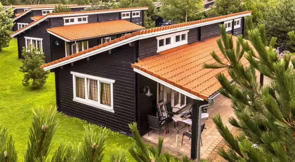 Czarny bungalow z pomarańczowym dachem, otoczony zielenią. To idealne miejsce na wypoczynek.