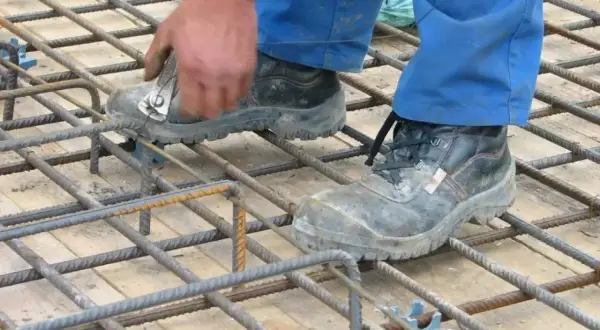 Pracownik w niebieskich spodniach i roboczych butach wiąże zbrojenie pod strop monolityczny.