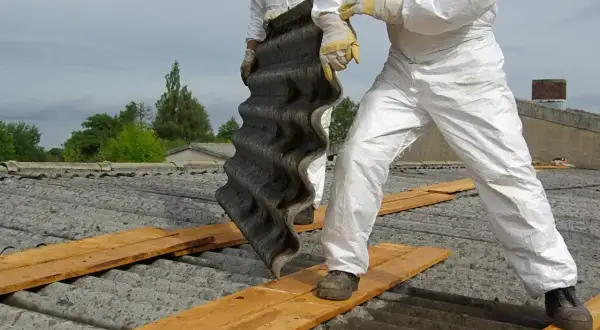 Osoby w kombinezonach ochronnych demontują eternit. Dowiedz się, ile kosztuje utylizacja eternitu i jak bezpiecznie usunąć ten materiał.