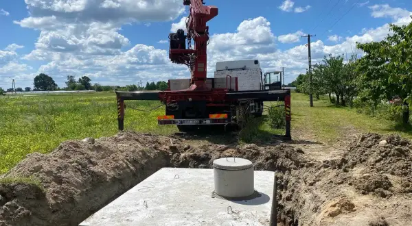 Montaż szamba betonowego w wykopie. Dźwig z ciężarówki przygotowuje się do pracy.