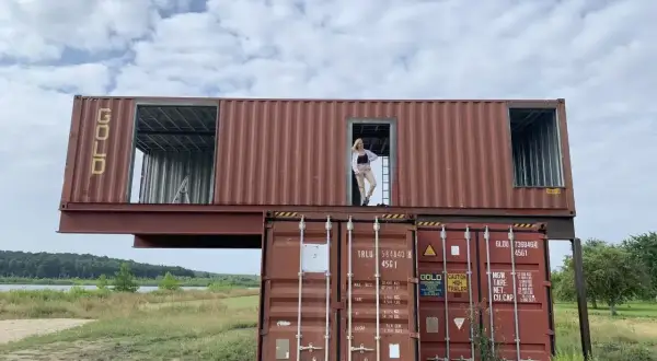 Dwupoziomowy dom z kontenerów 100m2 cena. Kobieta stoi w drzwiach górnego kontenera.