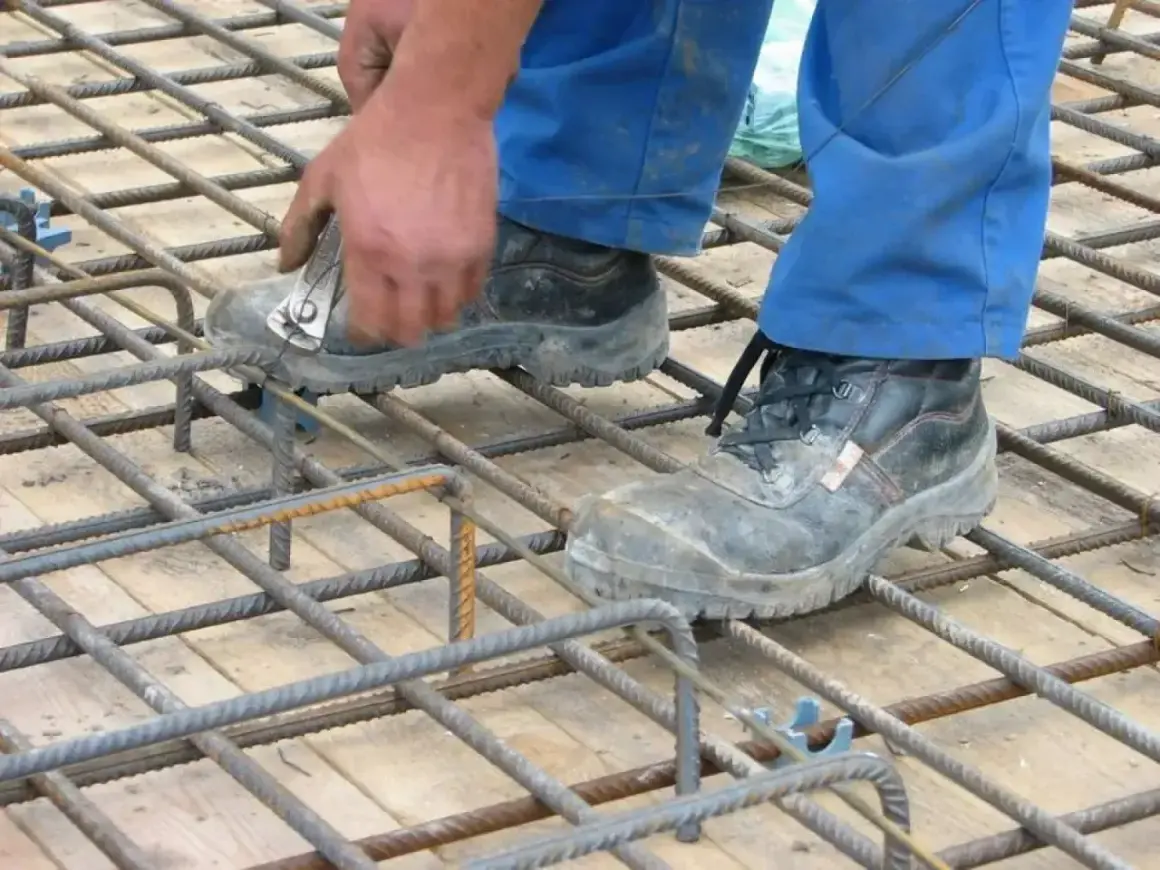 Pracownik w niebieskich spodniach i roboczych butach wiąże zbrojenie pod strop monolityczny.