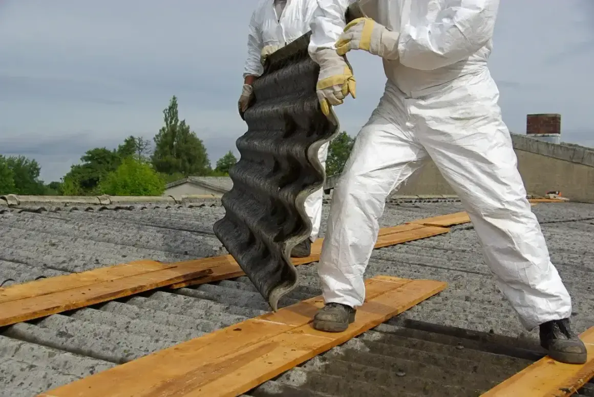 Osoby w kombinezonach ochronnych demontują eternit. Dowiedz się, ile kosztuje utylizacja eternitu i jak bezpiecznie usunąć ten materiał.