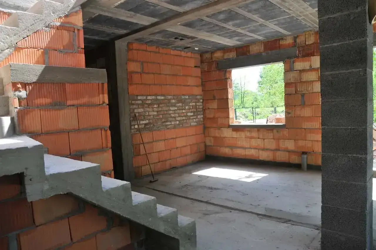 Wnętrze budującego się budynku wielorodzinnego. Widać schody, ściany z cegły i betonowy strop.