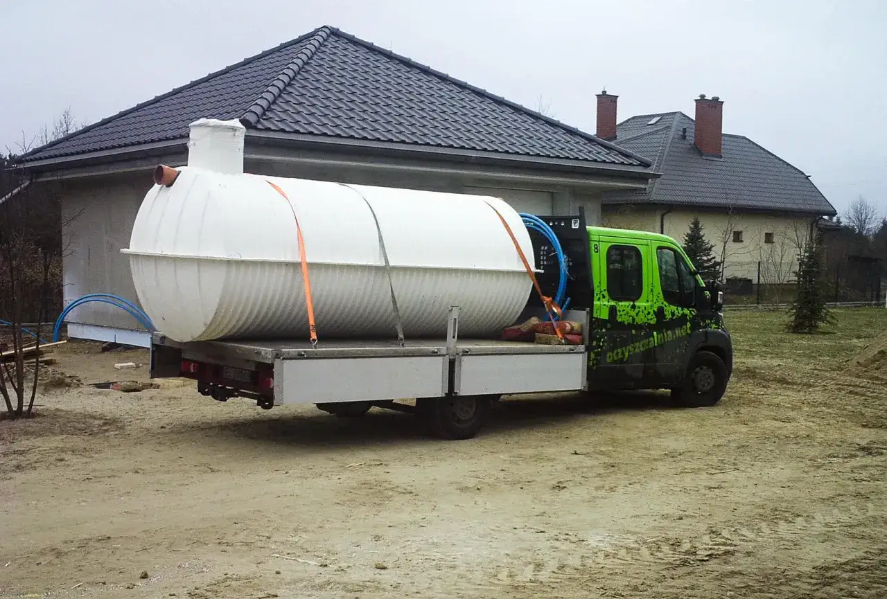 Dostawa białego, plastikowego szamba na przyczepie. Wybór między szambo betonowe czy plastikowe jest ważny dla Twojego domu.