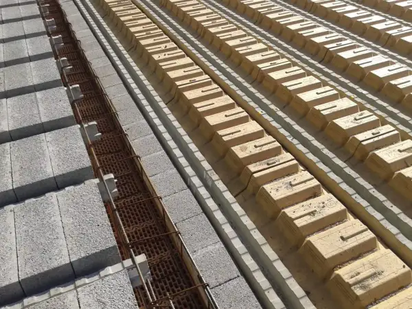 Budowa stropu: betonowe pustaki i zbrojenie w rowkach, obok żółte pustaki szalunkowe. Określanie grubości stropu.